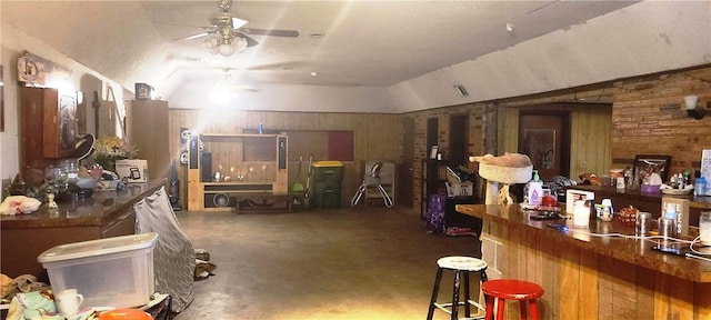 misc room with concrete flooring, ceiling fan, indoor bar, lofted ceiling, and wood walls