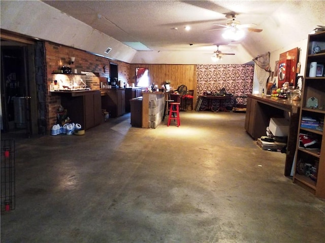 interior space with ceiling fan, wood walls, concrete flooring, a textured ceiling, and lofted ceiling