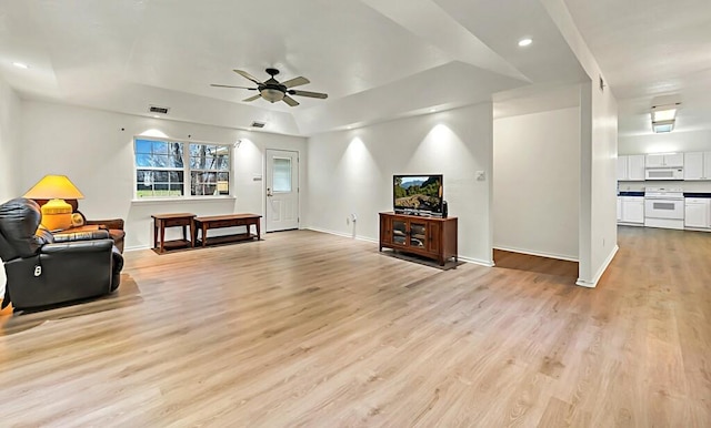 living room with ceiling fan, light hardwood / wood-style flooring, and a tray ceiling