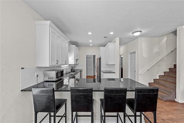 kitchen with white cabinetry, stainless steel appliances, kitchen peninsula, a kitchen bar, and hardwood / wood-style flooring