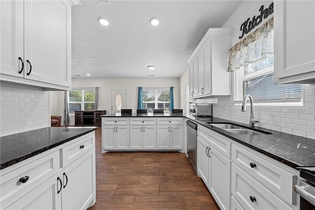 kitchen with stainless steel dishwasher, dark stone countertops, white cabinetry, and sink