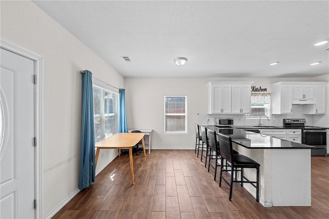 kitchen with stainless steel appliances, a kitchen breakfast bar, dark hardwood / wood-style flooring, a textured ceiling, and white cabinets