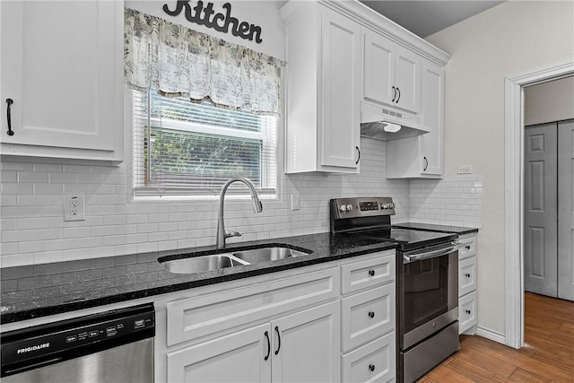 kitchen featuring appliances with stainless steel finishes, light wood-type flooring, sink, dark stone countertops, and white cabinetry