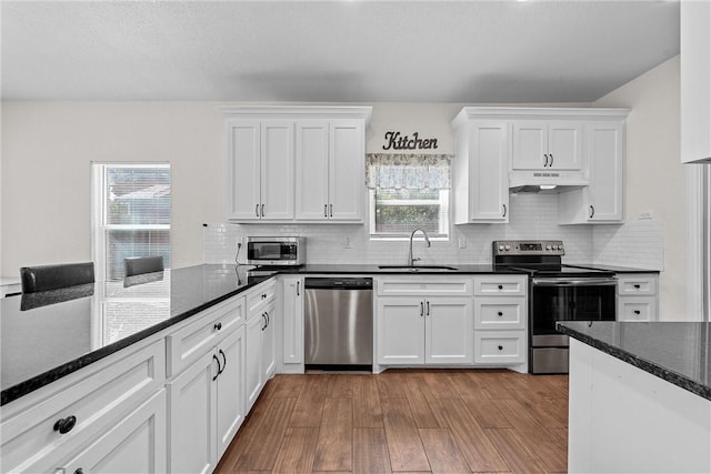 kitchen with sink, light hardwood / wood-style flooring, dark stone countertops, white cabinetry, and stainless steel appliances