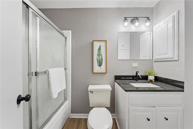 full bathroom with vanity, toilet, wood-type flooring, and bath / shower combo with glass door