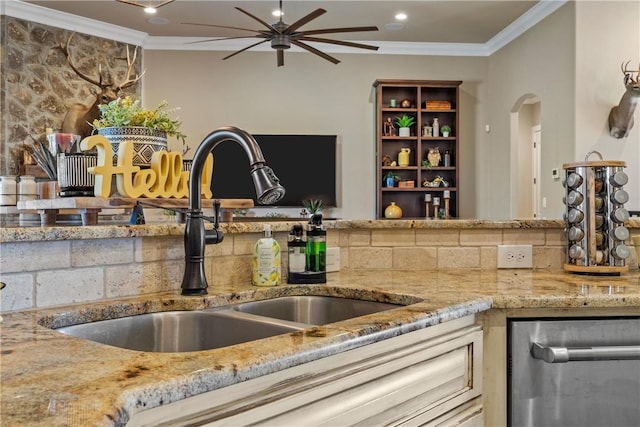 kitchen featuring arched walkways, ornamental molding, light stone countertops, and a sink