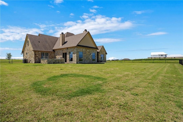 back of property with stone siding, fence, a yard, central AC unit, and a chimney