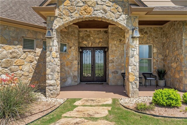 entrance to property with french doors, stone siding, and roof with shingles