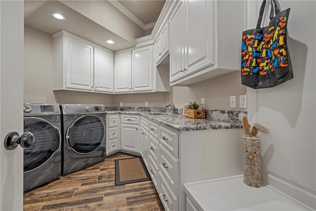 laundry area featuring wood tiled floor, washer and clothes dryer, ornamental molding, cabinet space, and a sink