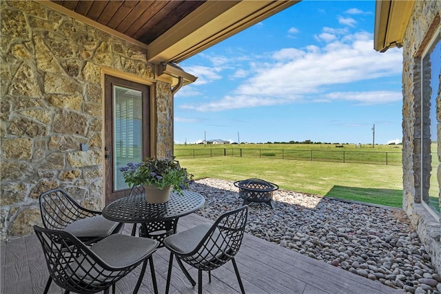 wooden terrace featuring a rural view, a lawn, a fire pit, and fence