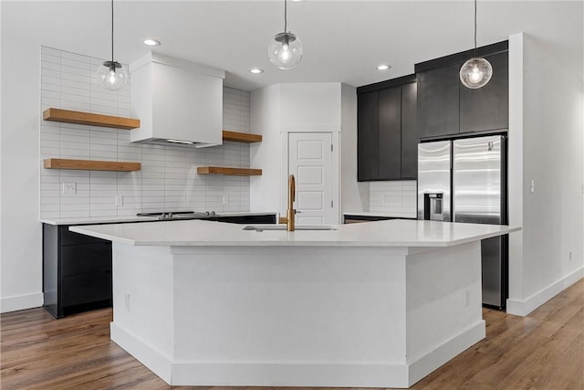 kitchen featuring sink, light hardwood / wood-style flooring, an island with sink, appliances with stainless steel finishes, and decorative light fixtures