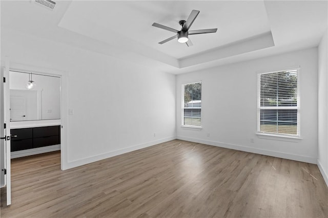 spare room with a tray ceiling, ceiling fan, and light hardwood / wood-style floors