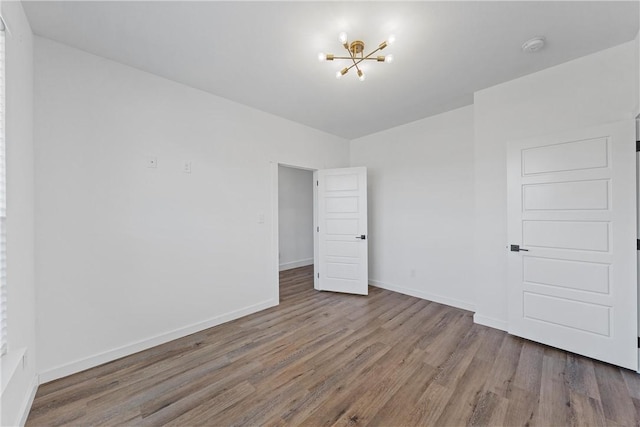 spare room with an inviting chandelier and hardwood / wood-style flooring