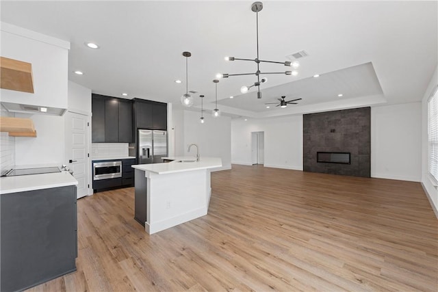 kitchen with hanging light fixtures, a fireplace, light hardwood / wood-style floors, and a center island with sink