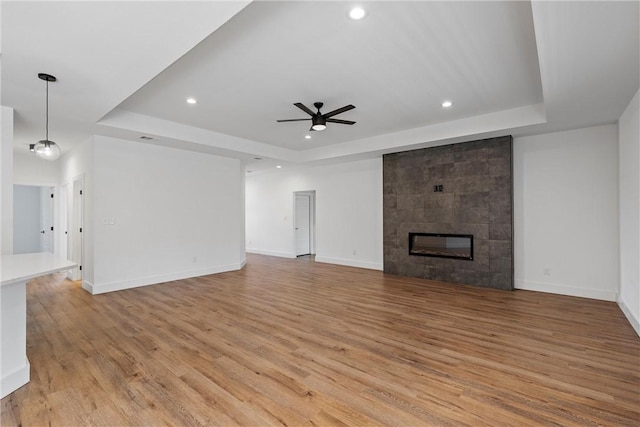 unfurnished living room with a tray ceiling, light hardwood / wood-style flooring, ceiling fan, and a tiled fireplace