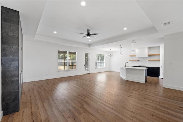 unfurnished living room featuring ceiling fan with notable chandelier, dark hardwood / wood-style flooring, a tray ceiling, and sink