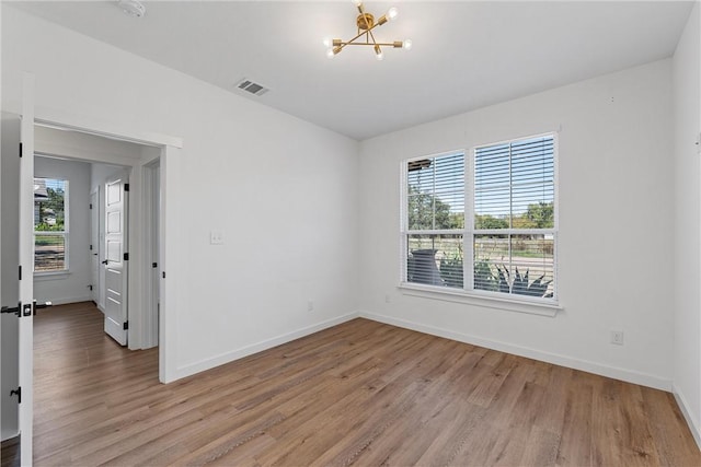 empty room featuring a notable chandelier and light hardwood / wood-style floors