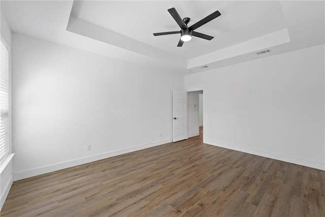 unfurnished room featuring a raised ceiling, a wealth of natural light, and hardwood / wood-style flooring