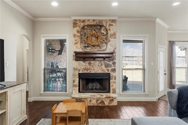 living area featuring arched walkways, a stone fireplace, dark wood-style floors, and ornamental molding