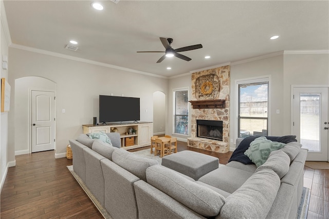 living area featuring a ceiling fan, visible vents, arched walkways, a stone fireplace, and dark wood-type flooring