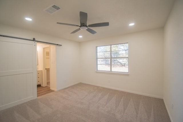 unfurnished bedroom with a barn door, carpet floors, ceiling fan, and connected bathroom