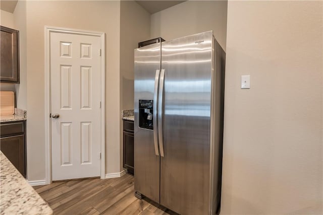 kitchen featuring light stone countertops, dark brown cabinets, stainless steel fridge, and light hardwood / wood-style flooring