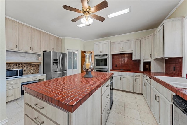 kitchen featuring tile counters, backsplash, crown molding, light tile patterned floors, and appliances with stainless steel finishes