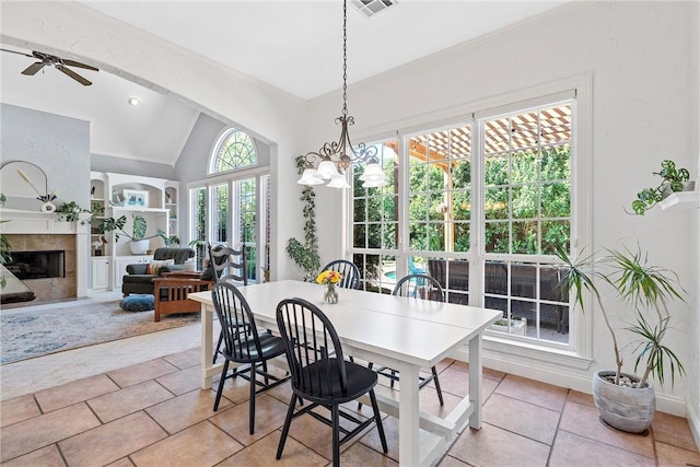 tiled dining area with ceiling fan with notable chandelier, a tiled fireplace, lofted ceiling, and built in shelves