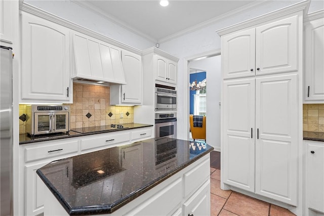 kitchen with stainless steel appliances, crown molding, light tile patterned floors, dark stone countertops, and white cabinetry