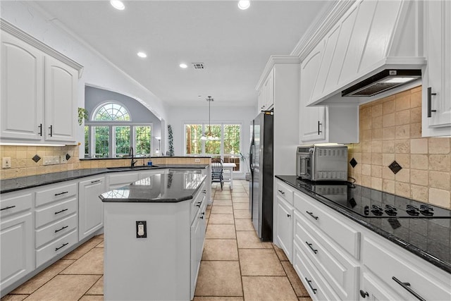 kitchen with black electric stovetop, dark stone counters, custom range hood, white cabinetry, and hanging light fixtures