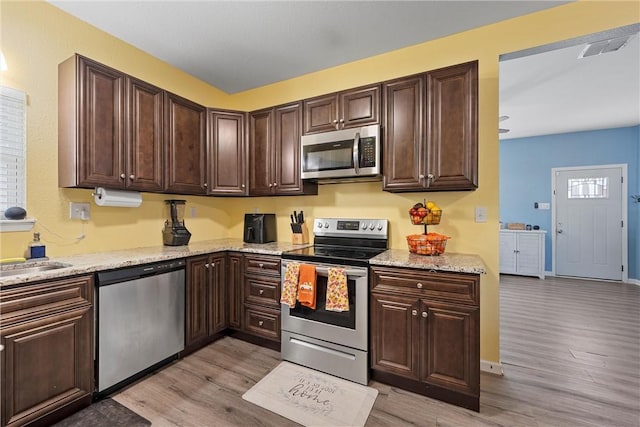 kitchen with light stone counters, dark brown cabinets, stainless steel appliances, and light wood-type flooring