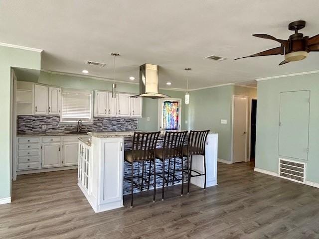 kitchen featuring pendant lighting, island exhaust hood, a kitchen island, and white cabinets