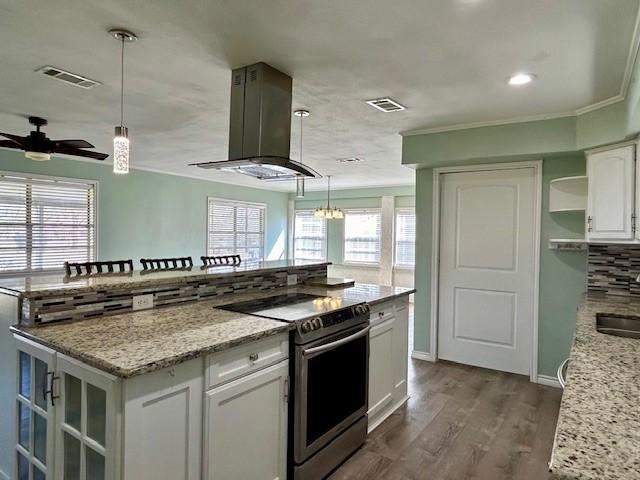 kitchen featuring white cabinetry, hanging light fixtures, island exhaust hood, light stone countertops, and stainless steel electric range