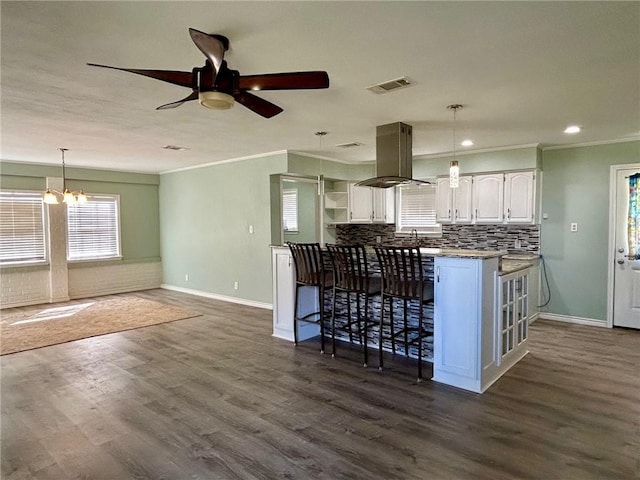 kitchen with a breakfast bar, white cabinetry, island range hood, dark hardwood / wood-style floors, and kitchen peninsula