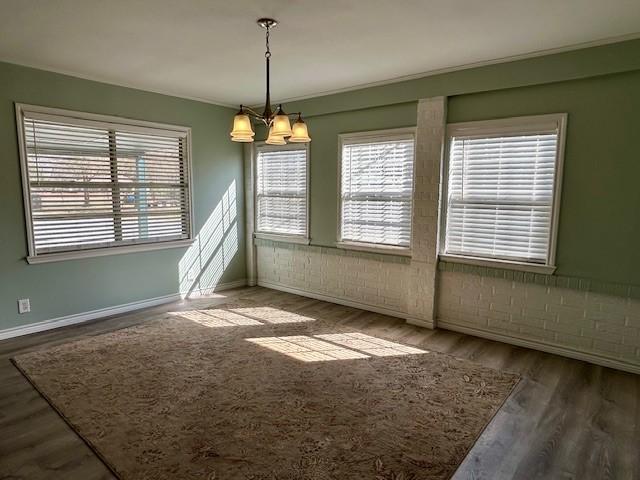 spare room featuring hardwood / wood-style flooring, a chandelier, and brick wall