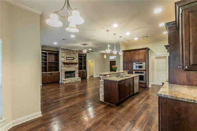 kitchen featuring a kitchen island with sink, sink, crown molding, decorative light fixtures, and dark hardwood / wood-style flooring