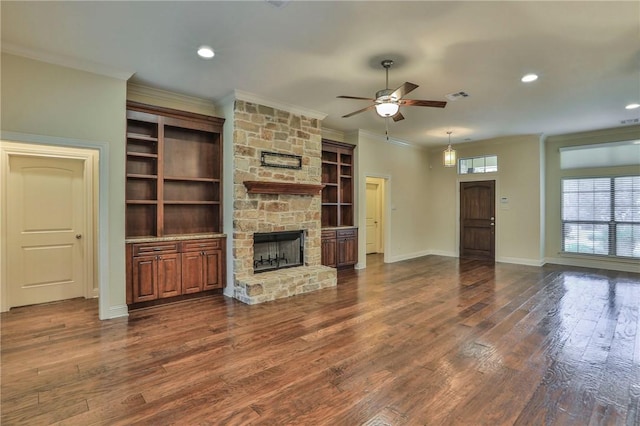 unfurnished living room featuring ceiling fan, a stone fireplace, ornamental molding, and dark wood-type flooring