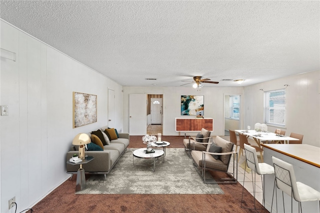 living room with ceiling fan, dark carpet, and a textured ceiling