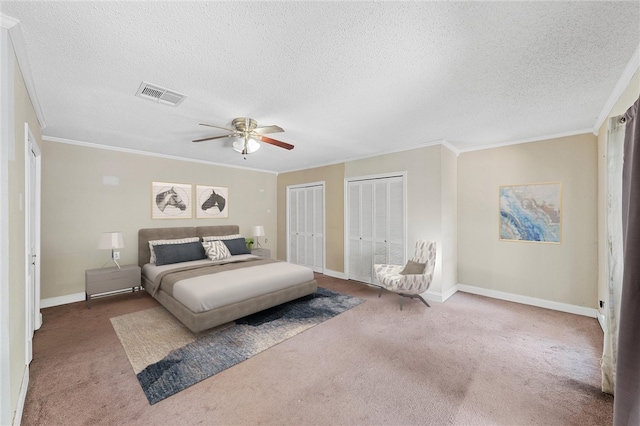 carpeted bedroom featuring ceiling fan, ornamental molding, a textured ceiling, and two closets