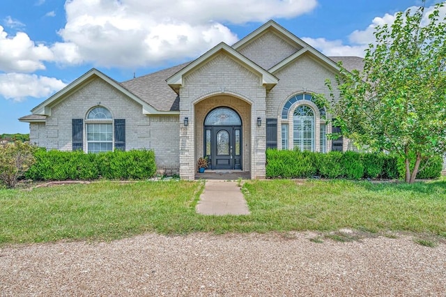 view of front of home with brick siding, a front lawn, and a shingled roof