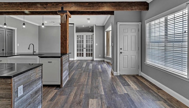 kitchen with baseboards, dark countertops, dark wood-style floors, a kitchen island with sink, and white cabinetry