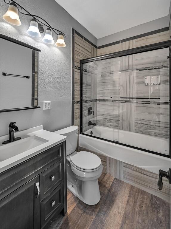 full bathroom featuring wood-type flooring, vanity, toilet, and enclosed tub / shower combo