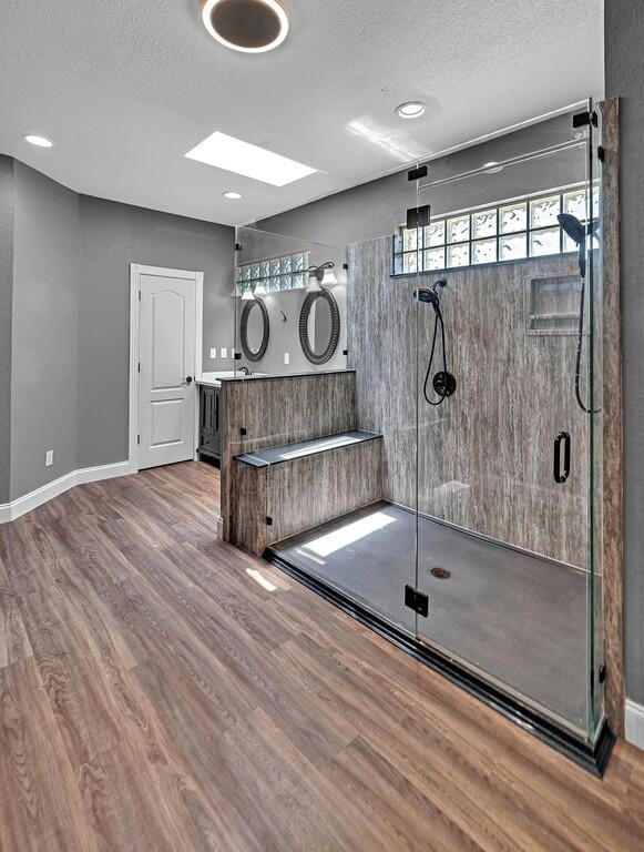 exercise area with a skylight, a textured ceiling, baseboards, and wood finished floors