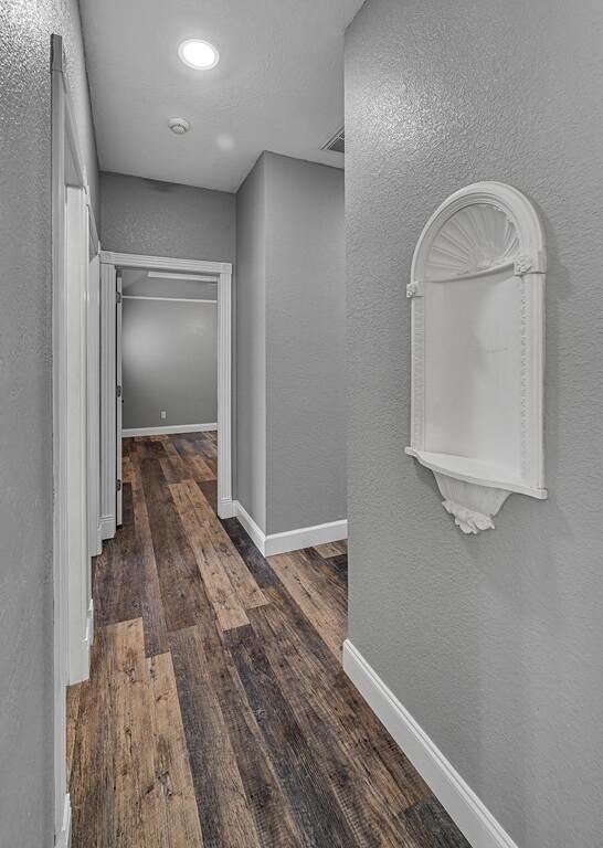 corridor with visible vents, a textured wall, baseboards, and wood finished floors