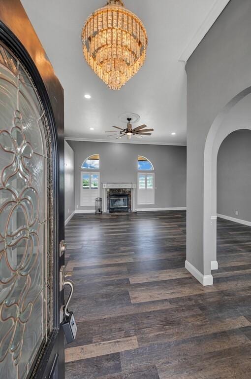 foyer with ceiling fan with notable chandelier, dark hardwood / wood-style flooring, ornamental molding, and a premium fireplace