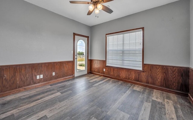 empty room featuring a ceiling fan, wainscoting, wood walls, and wood finished floors