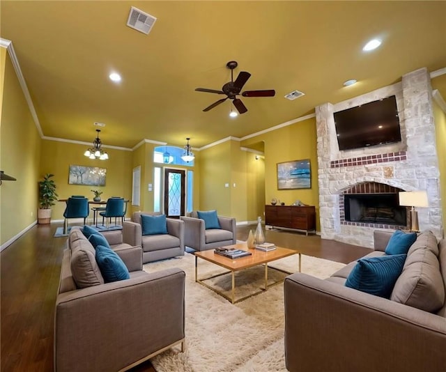 living area with wood finished floors, baseboards, visible vents, a stone fireplace, and ceiling fan with notable chandelier