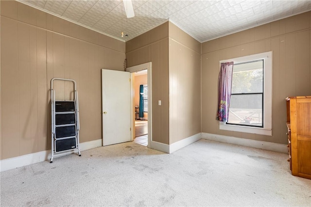 unfurnished bedroom featuring ceiling fan, wooden walls, and light colored carpet