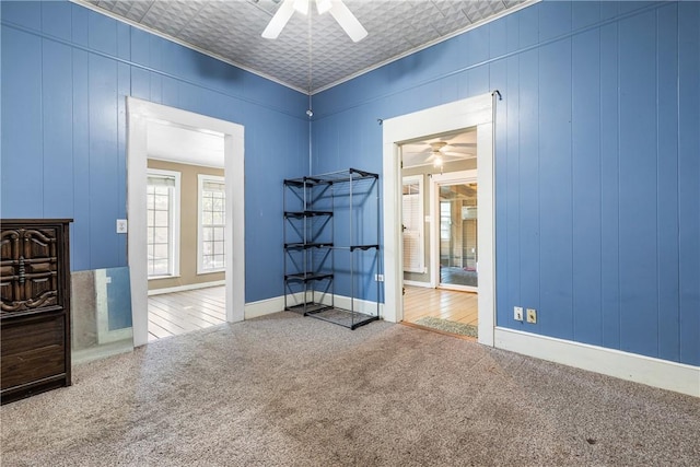 carpeted empty room featuring ceiling fan, crown molding, and wood walls