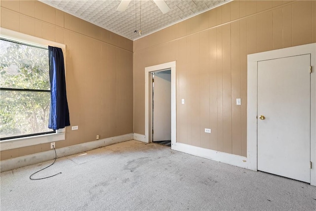 unfurnished bedroom featuring light carpet, wooden walls, and ceiling fan